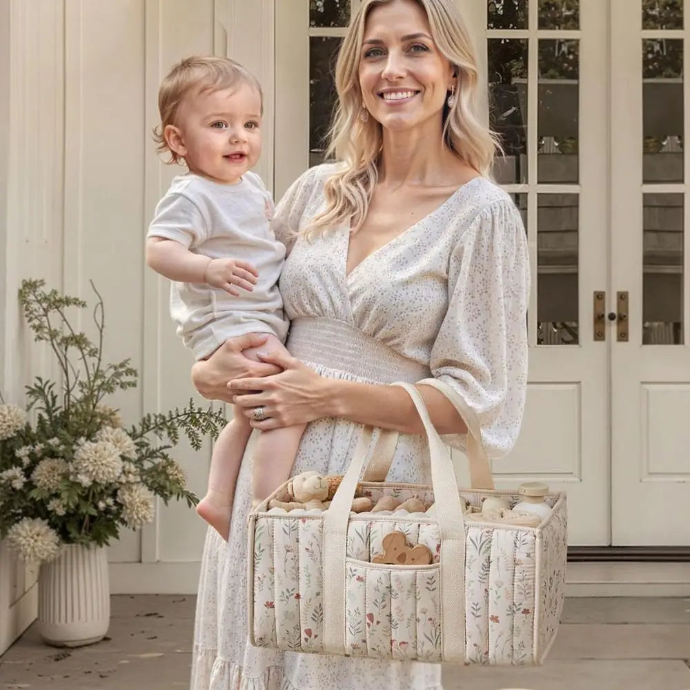 A woman holds a baby and carries a floral diaper organizer bag with multiple compartments.