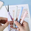 A hand holds several mini pen-shaped scissors and cutters in various pastel colors against a light background.