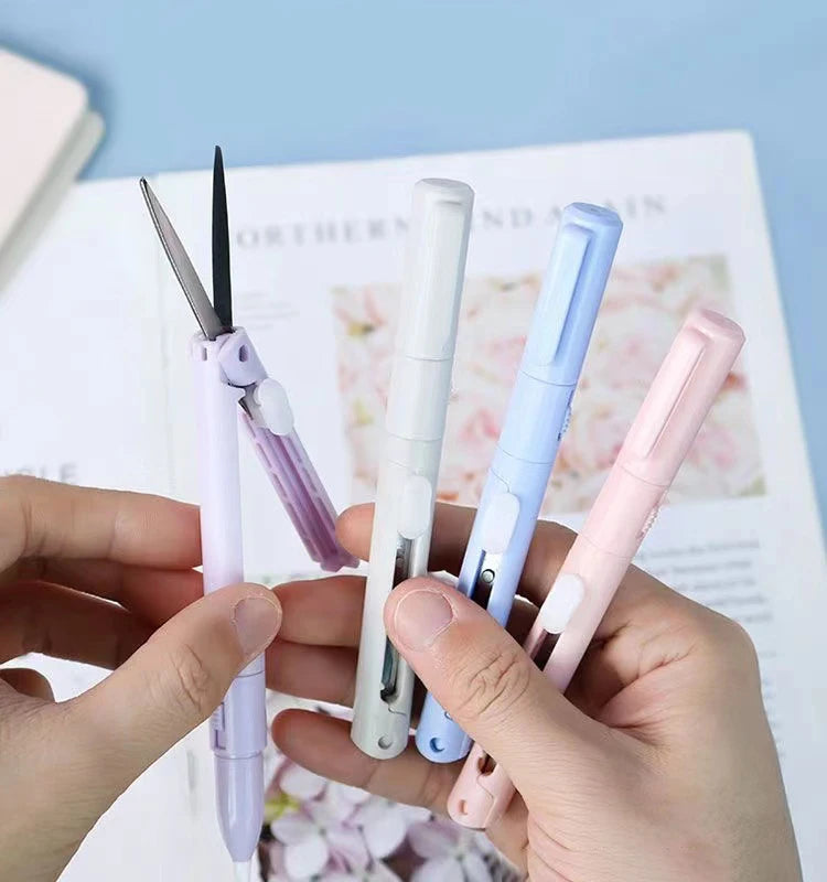 A hand holds several mini pen-shaped scissors and cutters in various pastel colors against a light background.