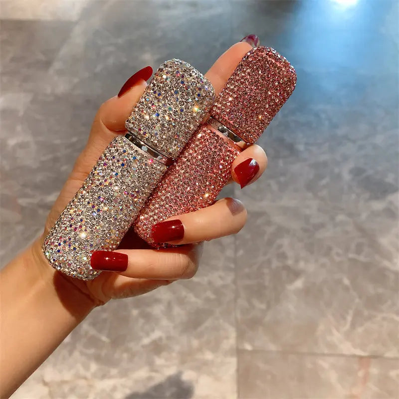 A hand holds three pink and silver refillable glass perfume atomizers with fine mist spray.