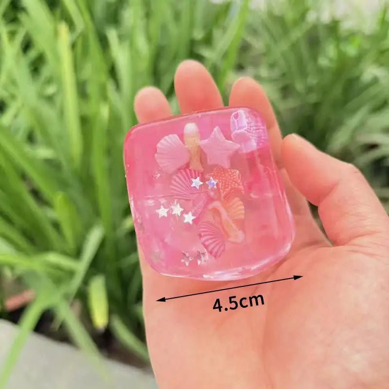 A hand holds a pink, translucent stress relief squeeze toy with an ocean theme featuring starfish and seashell designs.