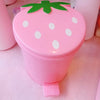 A pink strawberry-shaped mini trash can with a green leaf lid sits on a light surface.