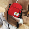 A red mini canvas crossbody bag with a gold tag is shown attached to a brown coat.