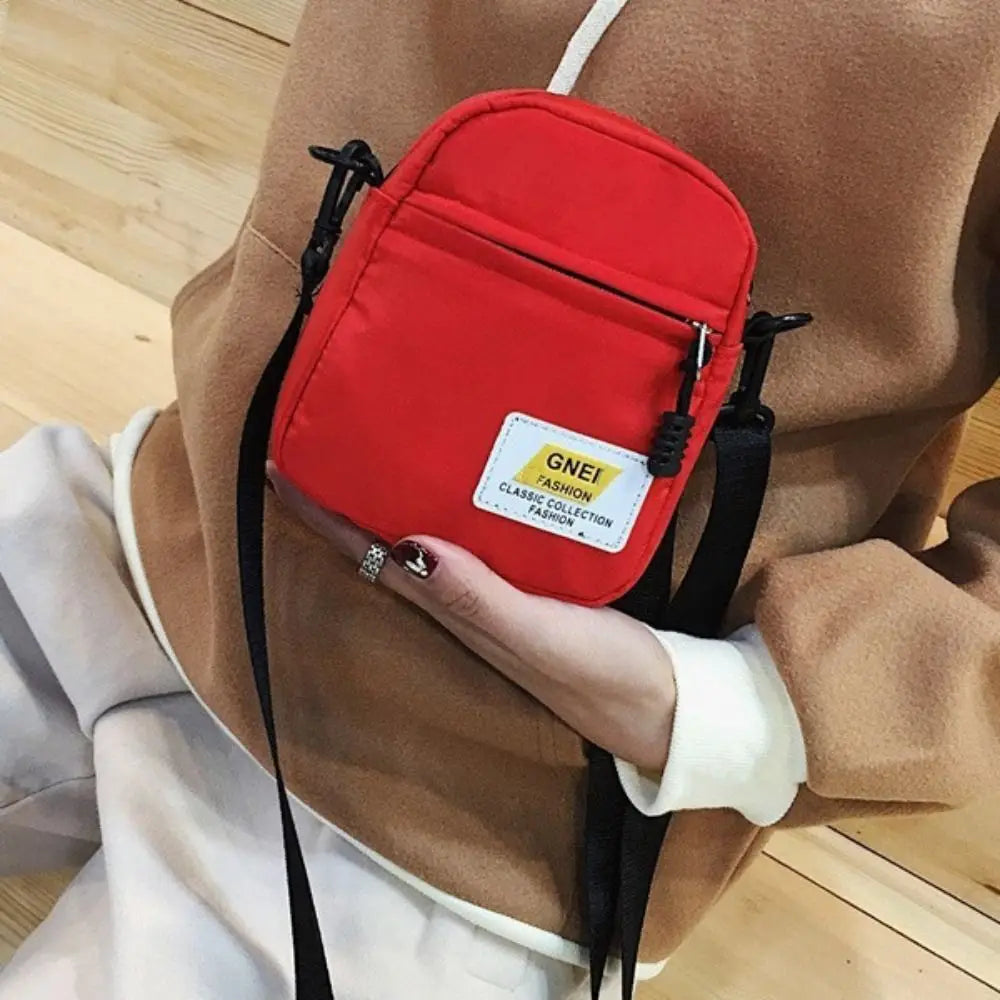 A red mini canvas crossbody bag with a gold tag is shown attached to a brown coat.