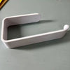 A white No-Drill Self-Adhesive Toilet Paper Holder with a curved design shown on a gray surface.