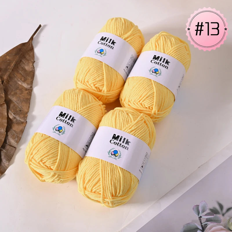 A stack of bright yellow Milk Cotton yarn balls for knitting and crochet, shown next to a dried leaf.
