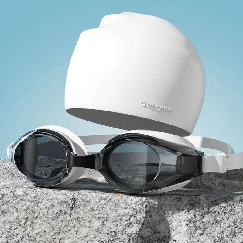 Gafas de natación blancas HD antiempañamiento con sello de silicona sobre una roca gris.