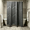 A dark gray bohemian floral cutout tassel shower curtain hanging on a rod in a bathroom.