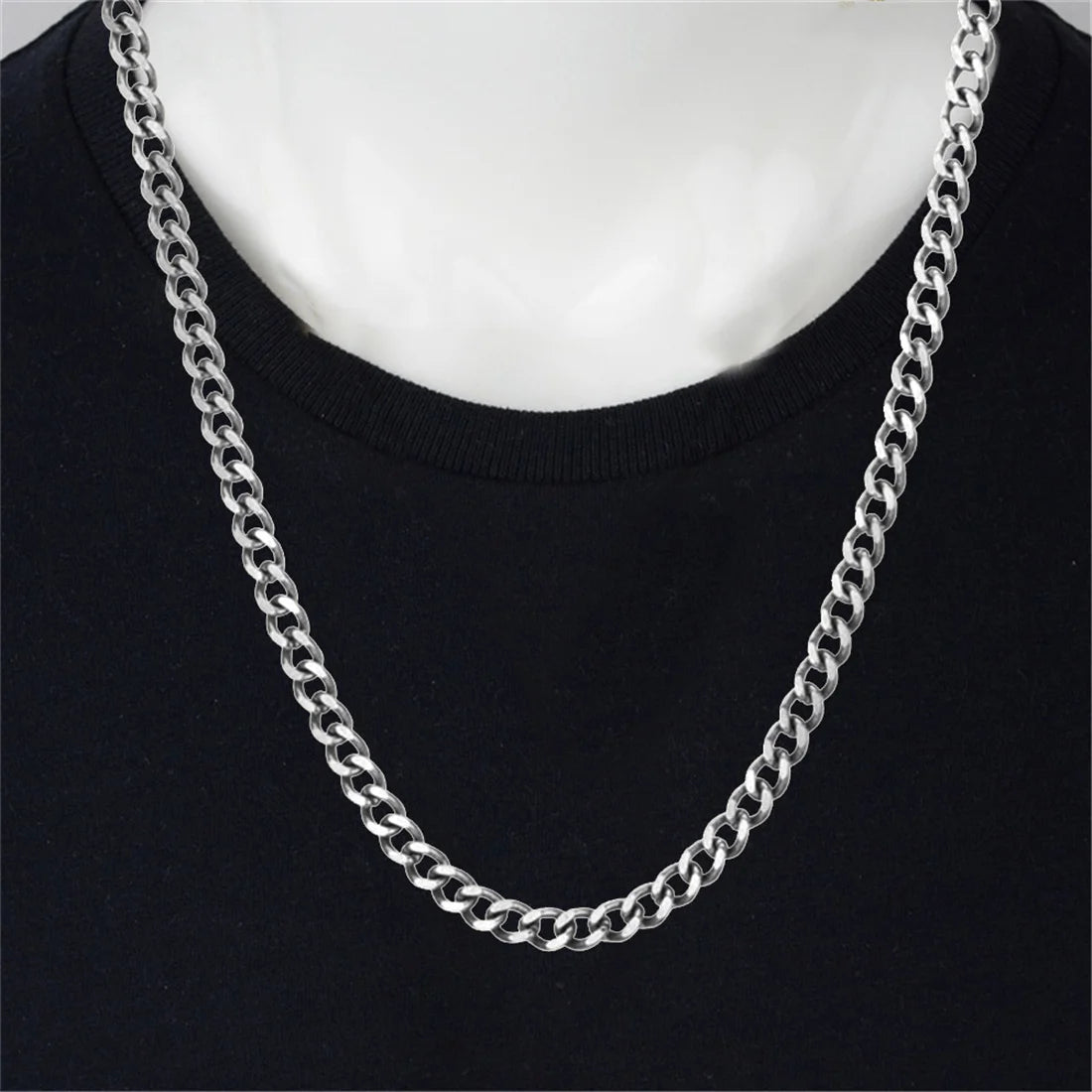 Silver stainless steel Cuban link chain necklace worn around the neck against a black shirt.