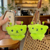 A bright lime green alien plush charm with small antennae is attached to a leather keychain and displayed next to a woven bag