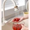 A kitchen faucet sprayer is shown spraying water onto fresh tomatoes.