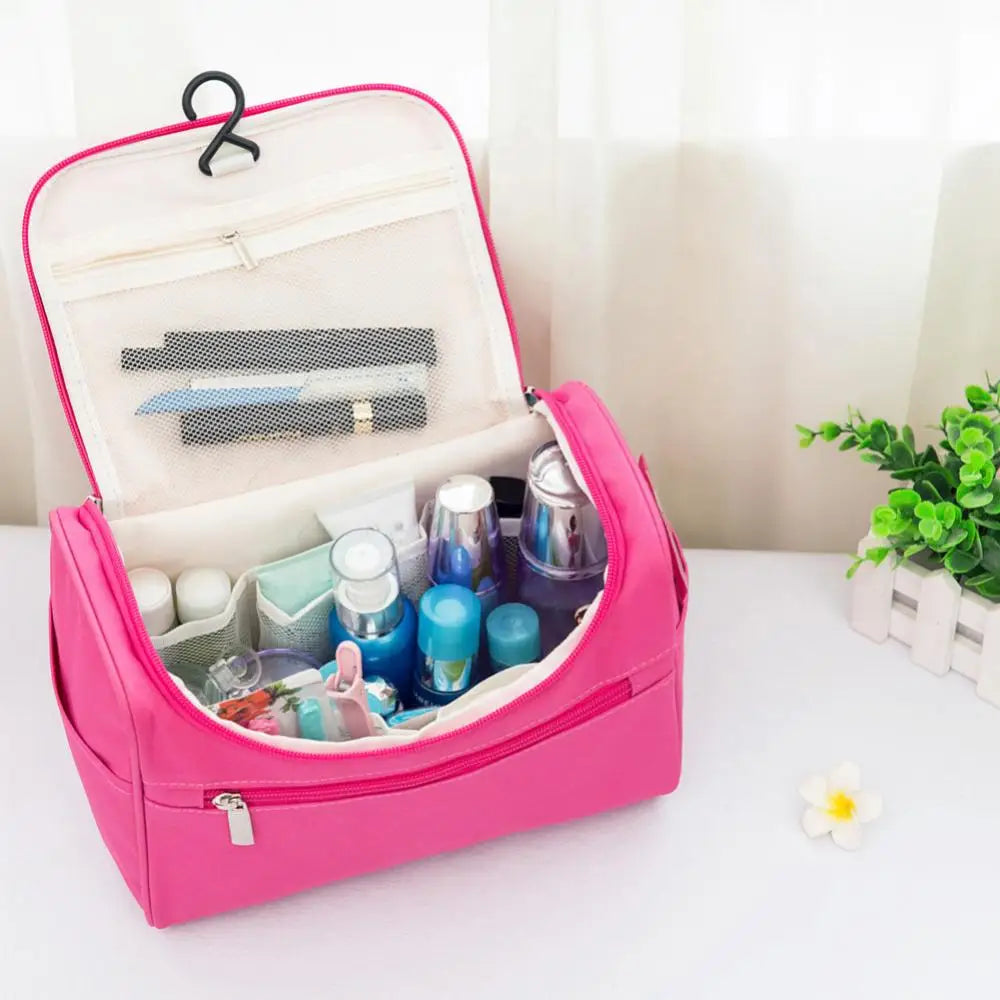 A pink hanging makeup bag is open, showing various cosmetic products inside on a white surface.