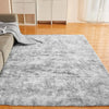 Flauschtiger grauer Tie-Dye-Teppich auf einem Holzfußboden in einem hellen Raum.