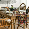 A wooden dining table set for a meal featuring a colorful Day of the Dead table runner with skull and floral designs.