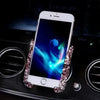 A white phone is held in a crystal air vent car phone holder on a dark surface.