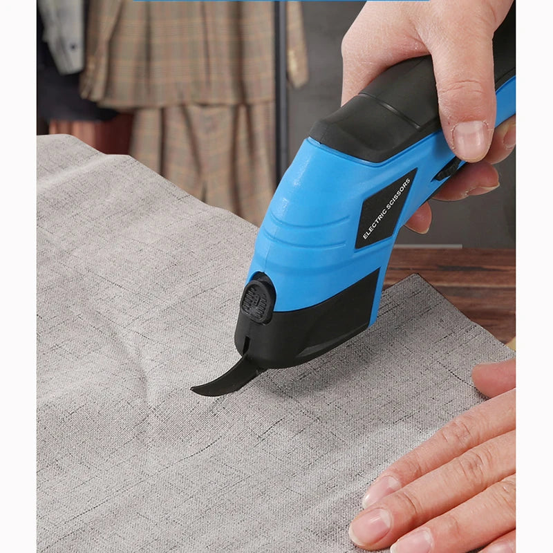 A hand holds a blue and black cordless electric scissor tool used for cutting fabric or other materials.