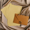 A set of yellow lined paper sheets and an orange envelope with a gold sealing wax sticker placed on draped fabric.