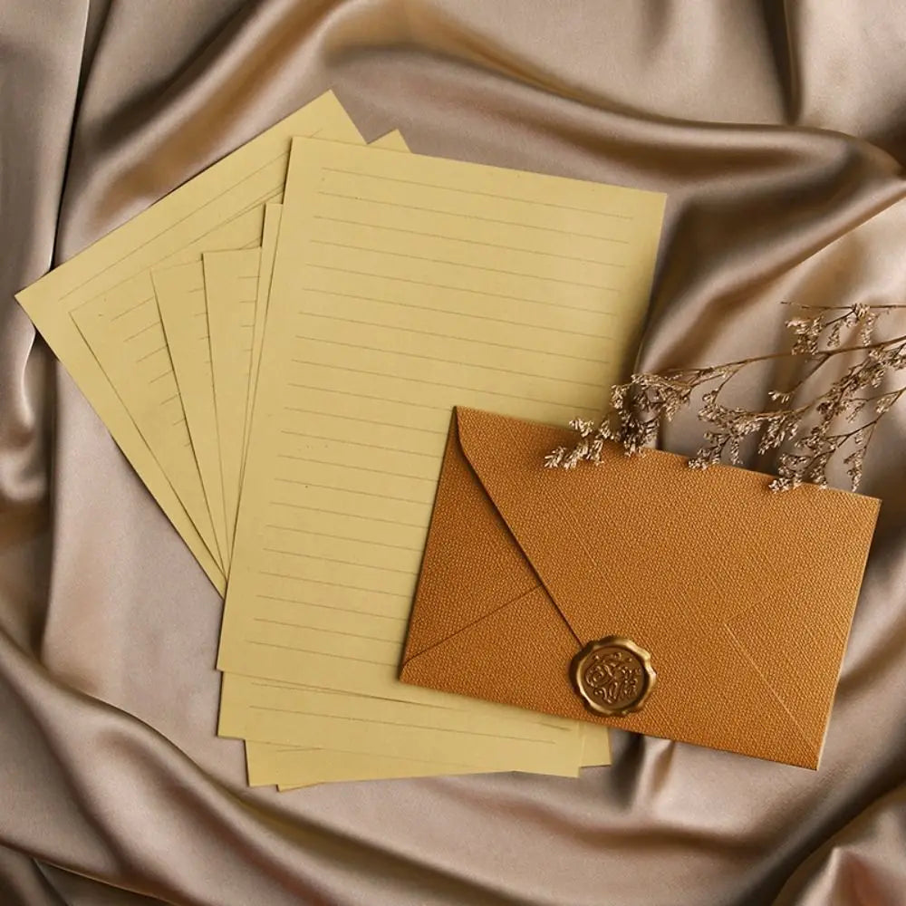 A set of yellow lined paper sheets and an orange envelope with a gold sealing wax sticker placed on draped fabric.