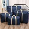 A set of navy blue waterproof moving and storage bags with tan straps are displayed on a wooden floor.