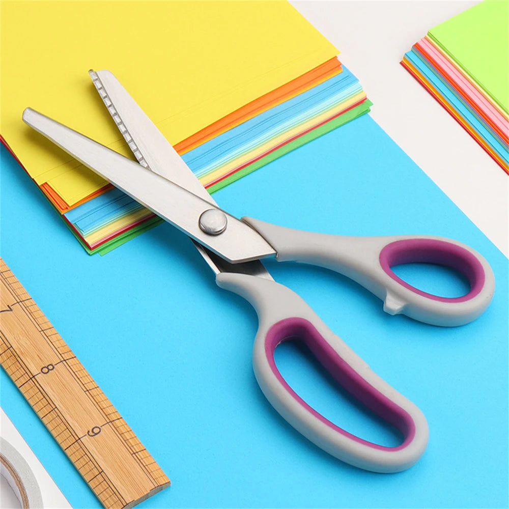 A pair of professional pinking shears with stainless steel blades resting on a blue surface next to colorful paper and a rule