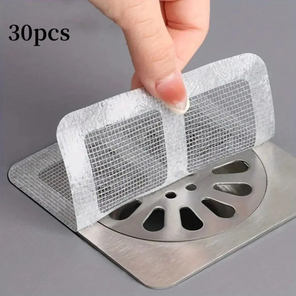A hand is placing a disposable drain hair catcher sticker onto a metal drain grate.