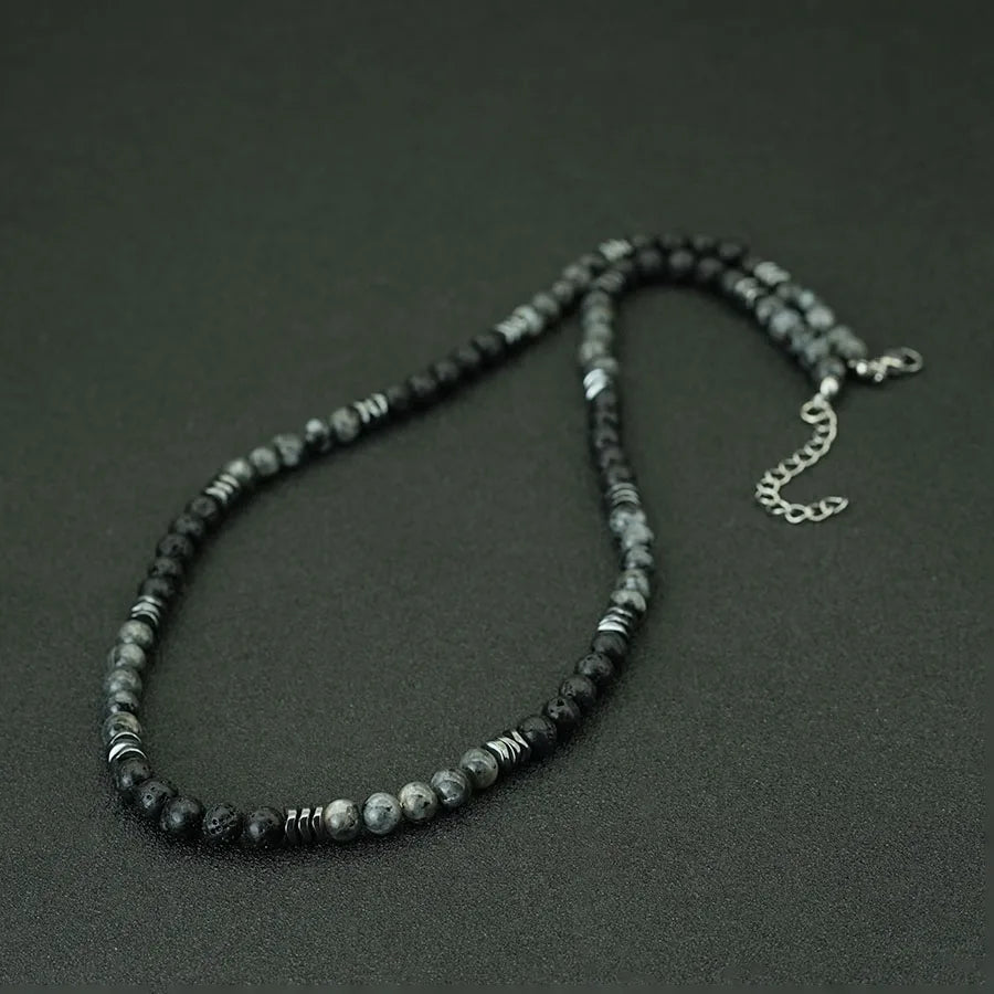 A dark beaded necklace made of Tiger's Eye and lava stones laid on a dark surface.