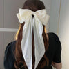A woman with long brown hair tied in a ponytail wearing a large white silk bow hair clip.