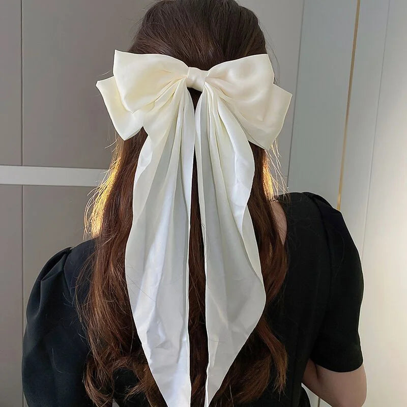 A woman with long brown hair tied in a ponytail wearing a large white silk bow hair clip.