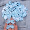 A hand holds several light blue embroidered cartoon bow iron-on patches on a denim fabric background.