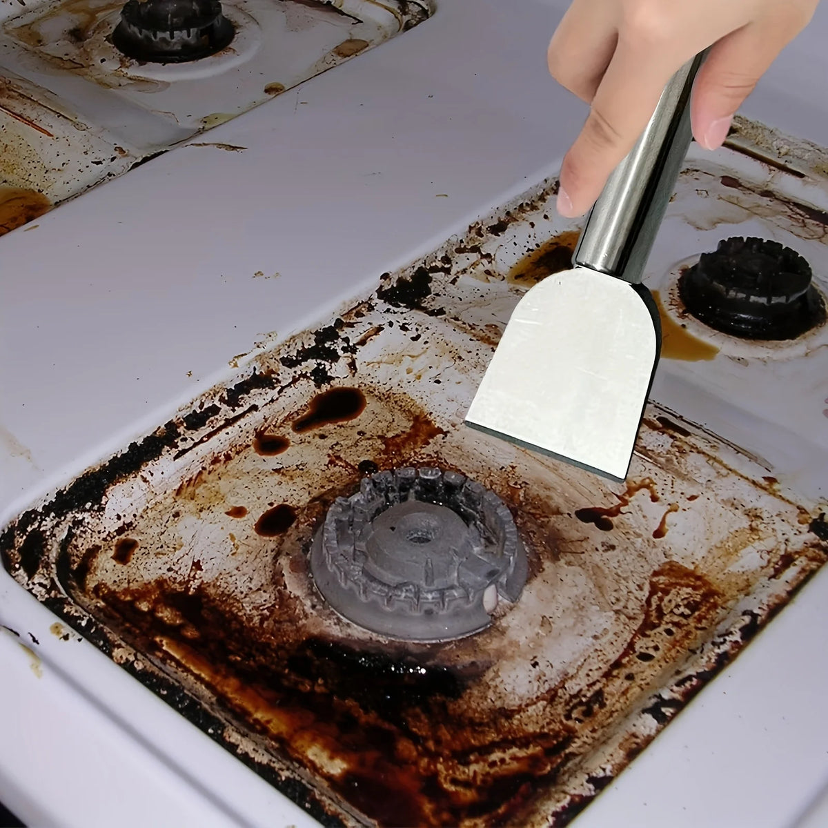 A hand uses a stainless steel scraper to remove residue from a cooking pan or surface.