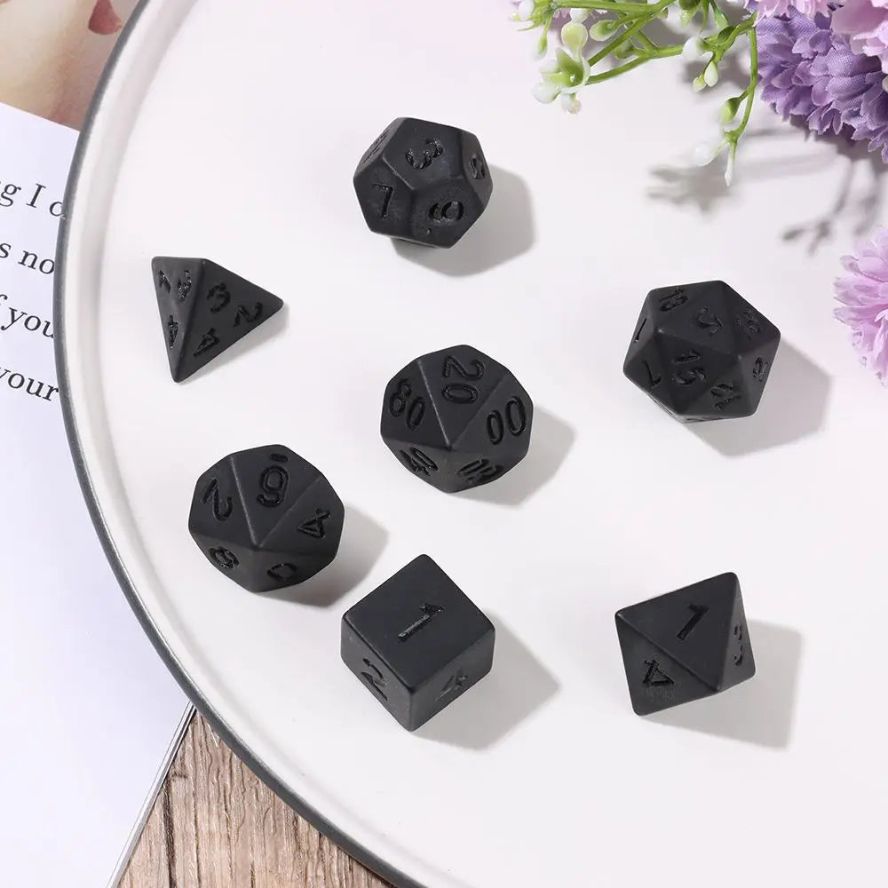 A set of matte black polyhedral dice, including d10s and d20s, arranged on a white plate.