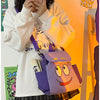 Eine Person hält einen lila und gelben Dora The Explorer Flanell-Rucksack vor einem orangefarbenen Hintergrund.