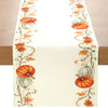 A cream table runner featuring an autumnal design with orange pumpkins and golden leaves.
