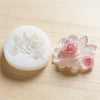 Un moule en silicone en forme de rose rose est exposé sur une surface en bois clair.