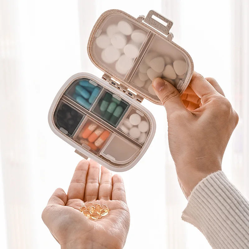 A hand opens a weekly pill organizer with eight compartments filled with white and colored pills.