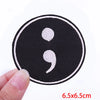 Black embroidered iron-on letter patch with white characters being held by a hand