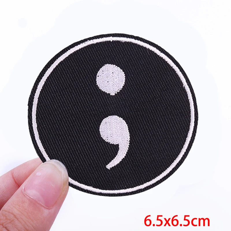 Black embroidered iron-on letter patch with white characters being held by a hand
