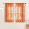 Orange sheer curtains with pom pom detailing and 3D jacquard rod pockets hanging in a window.