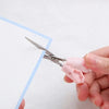 A hand holds a pair of stainless steel cat paw portable scissors against a white sheet of paper.
