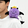 A purple plush doll with a yellow crown and black wings is displayed on a person's shoulder.