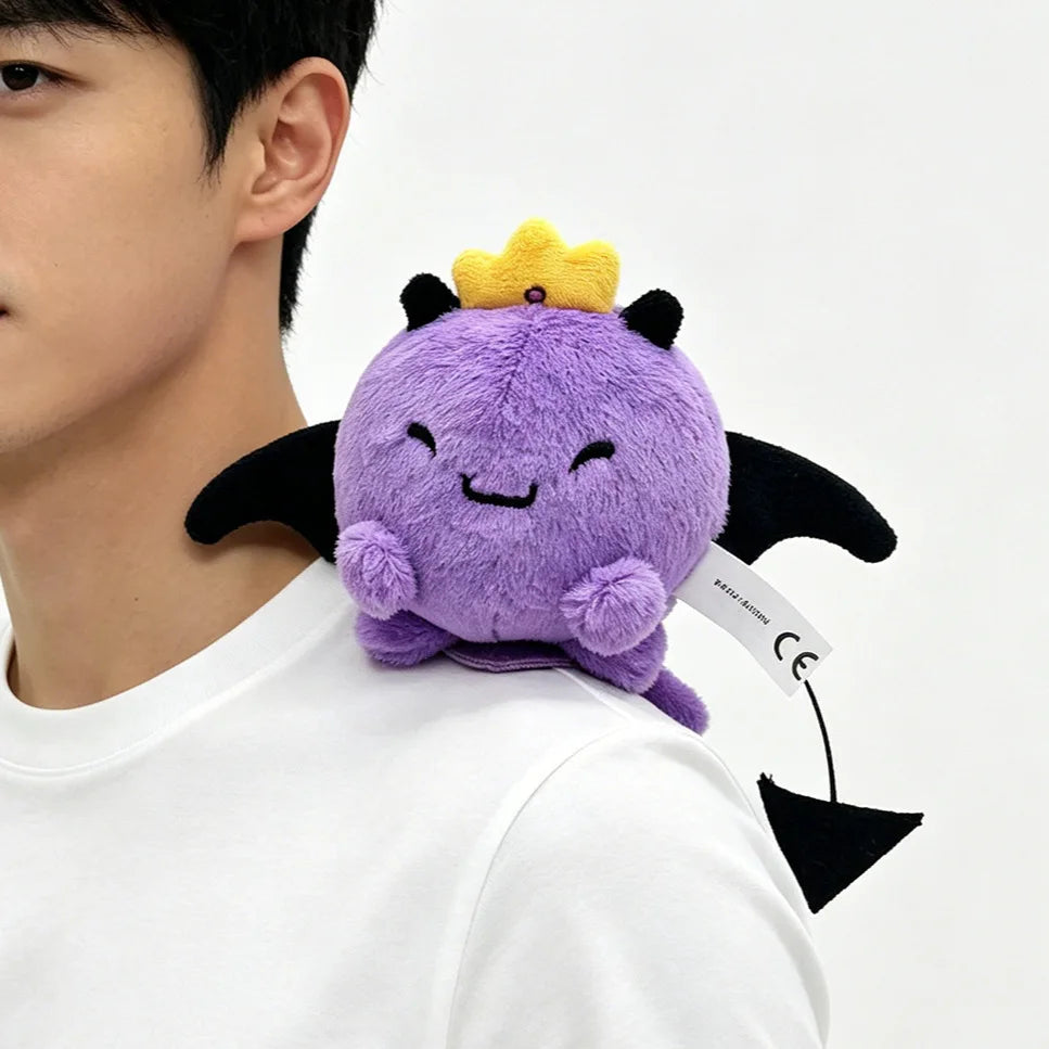 A purple plush doll with a yellow crown and black wings is displayed on a person's shoulder.
