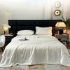 A white lightweight ice silk quilt is displayed on a bed with a black headboard and modern lighting.