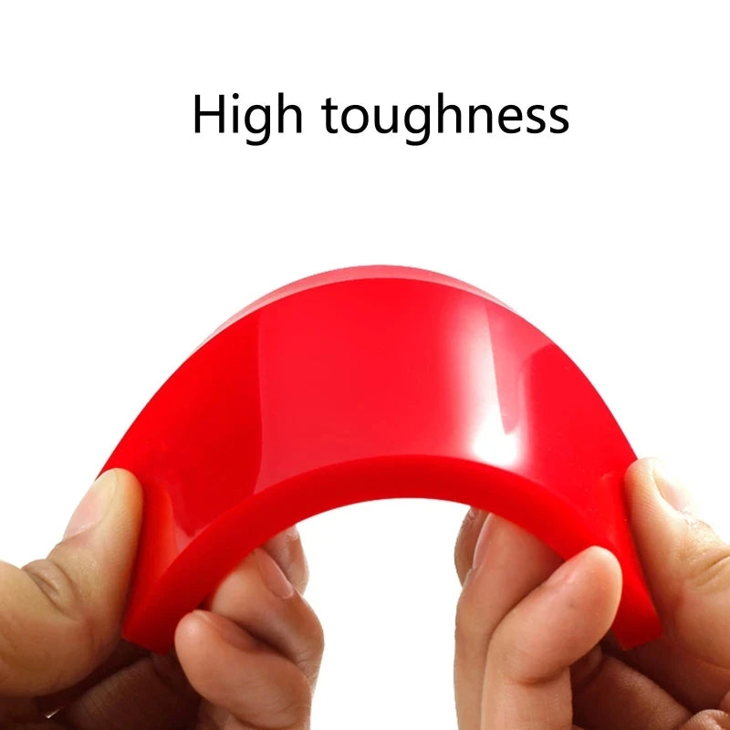 A hand holds a bright red car window squeegee with a soft rubber blade.
