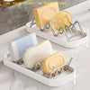 A set of W-shaped stainless steel soap holders with drainage trays in yellow and white on a marble surface.