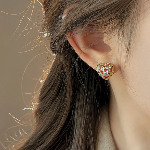 Gros plan sur l'oreille d'une femme avec de délicats clous à cœur en or et pierres roses.