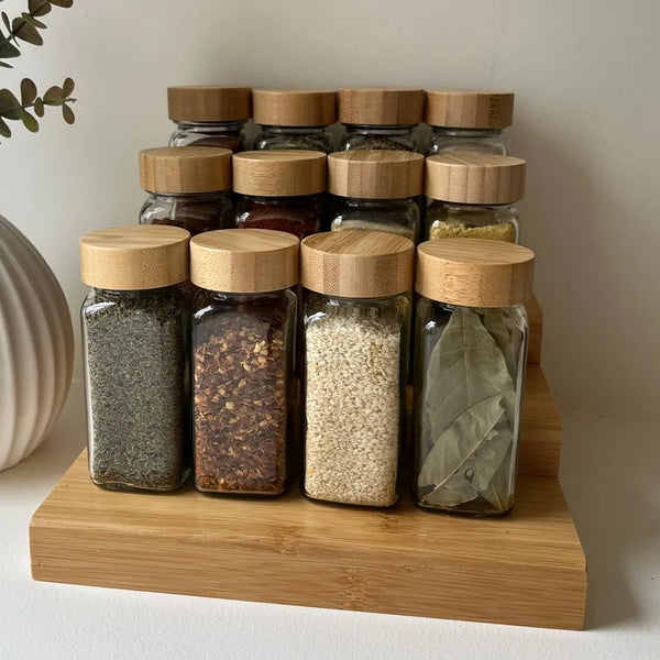 Une rangée de bocaux en verre transparent avec couvercles en bambou remplis d'épices moulues, disposés sur une planche en boi