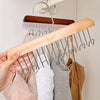 A hand holds a wooden hanging clothes rack with multiple metal hooks against a white wall.
