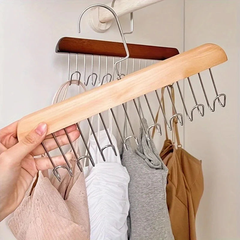 A hand holds a wooden hanging clothes rack with multiple metal hooks against a white wall.