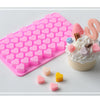 A pink silicone mold tray filled with heart-shaped cavities, next to a cupcake decoration made of pink and brown elements.