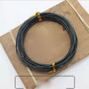 Black anodized aluminum jewelry wire coiled on a wooden board with natural twine.